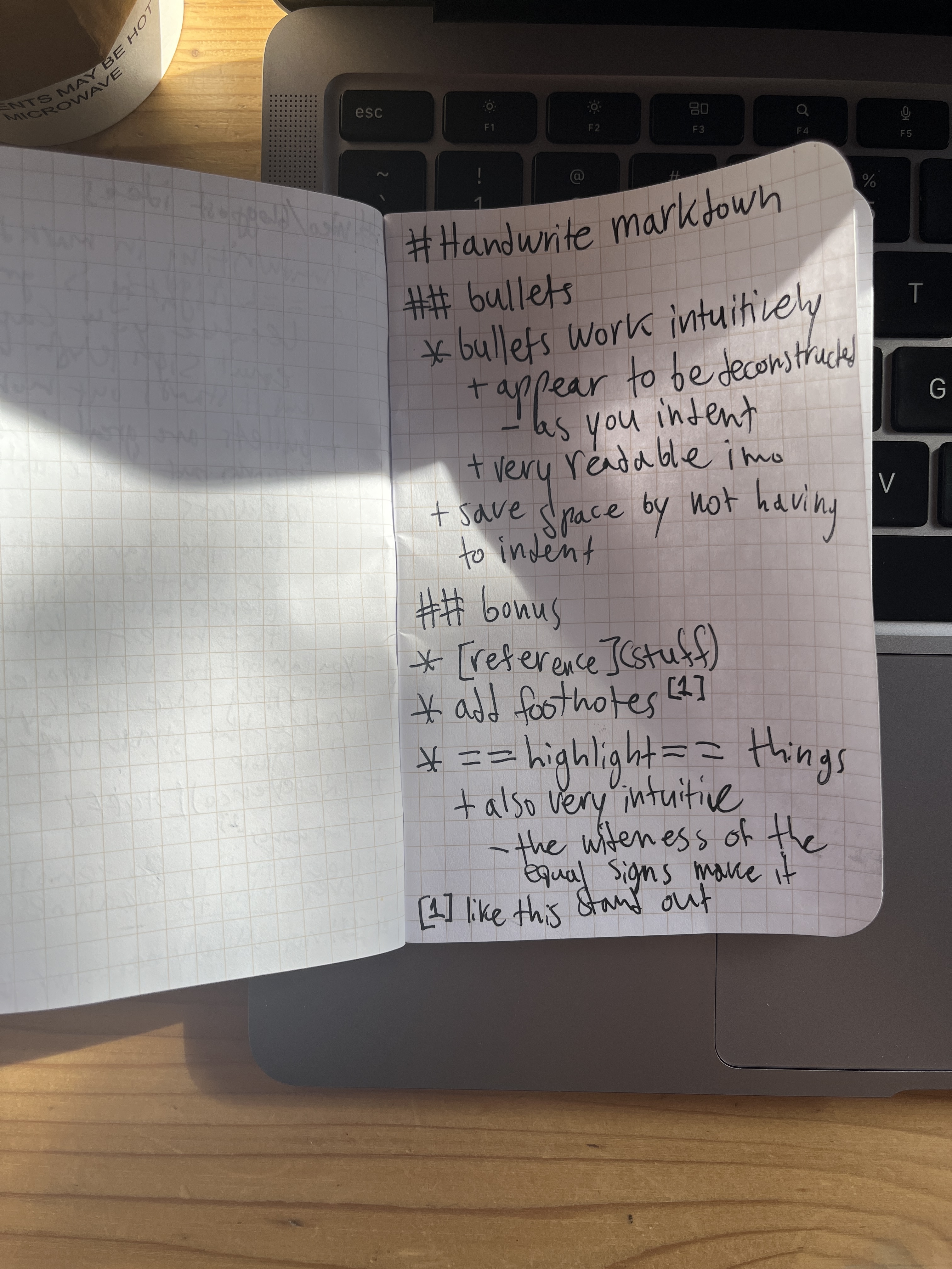 A handwritten note on grid paper demonstrating Inkdown features, placed on a laptop keyboard, with sunlight casting shadows across the page.