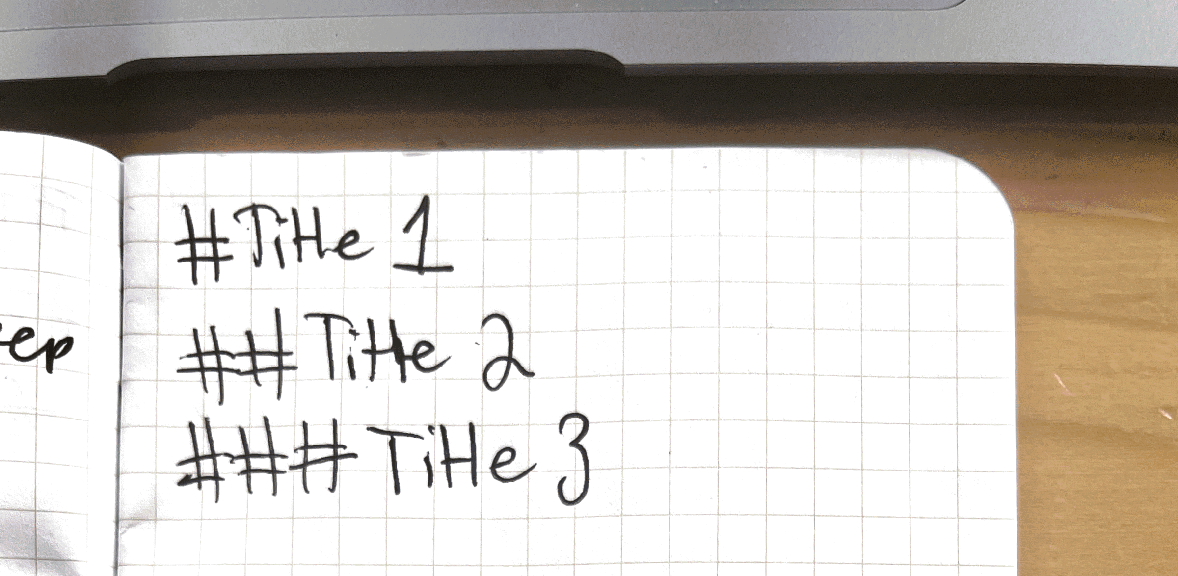 Close-up photo of a handwritten note on grid paper: #Title 1, ##Title 2, and ###Title 3 on seperate lines